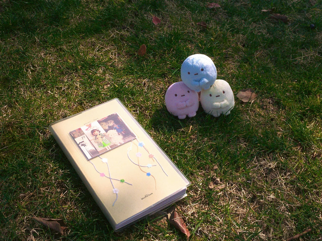 Yellow journal with floral illustration and photo collage cover resting on grass beside three plush toys