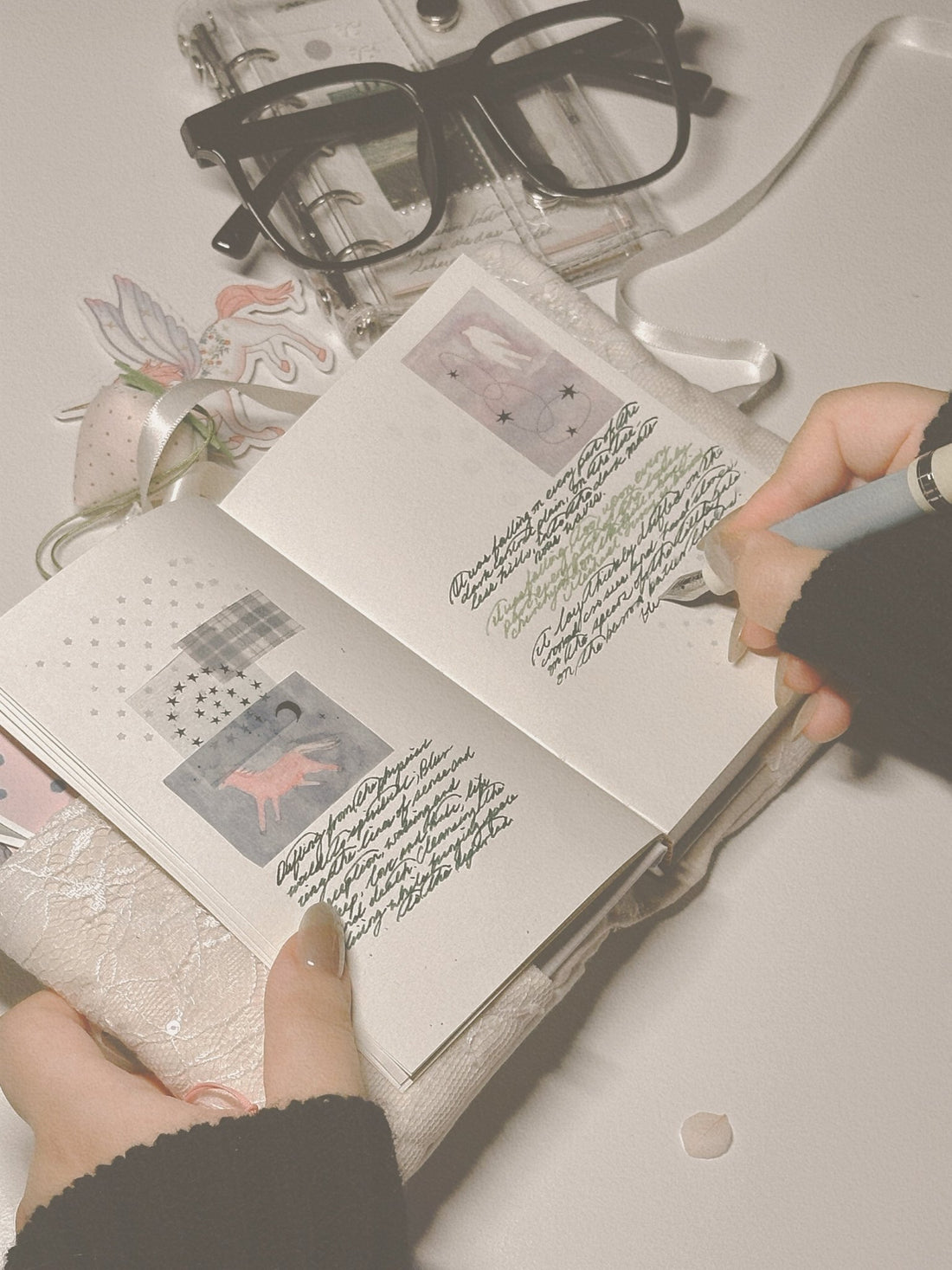 Hands writing in a small, lace-covered journal with star and animal stickers, with black-framed glasses nearby.