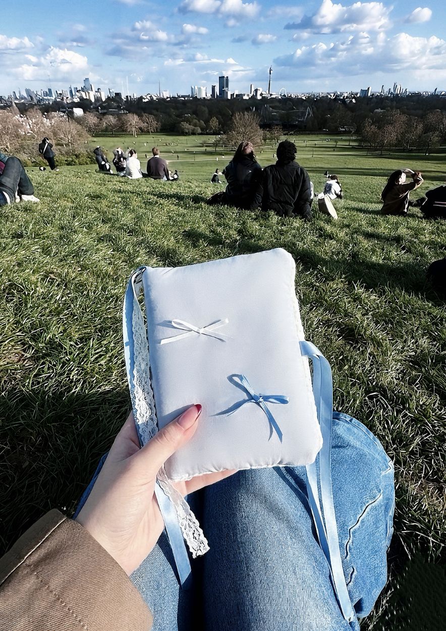 A person sitting on a grassy hill with a light blue vintage-inspired Kuura journal resting on their lap. 