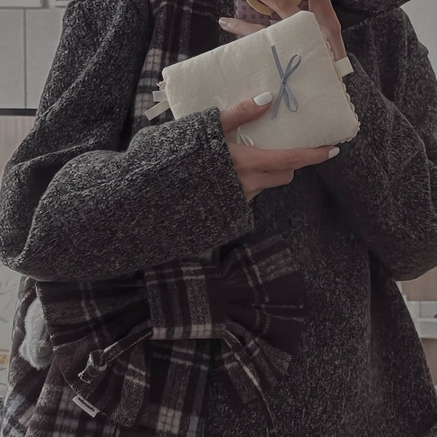 Hands holding a Kuura journal cover wrapped in cream fabric and tied with a light blue ribbon, styled with a cozy plaid outfit