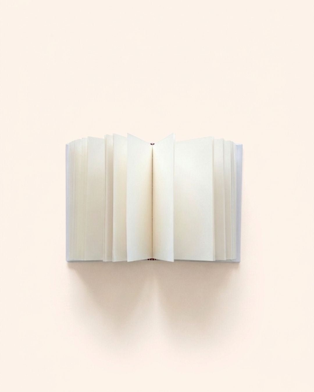 Close-up overhead photograph of Kuura's A5 and A6 Unlined Hardcover Notebook opened flat, showing fanned-out, thick, premium creamy blank pages. A minimalist, bleed-resistant journal base for fountain pen friendly writing, sketching, and memory keeping.