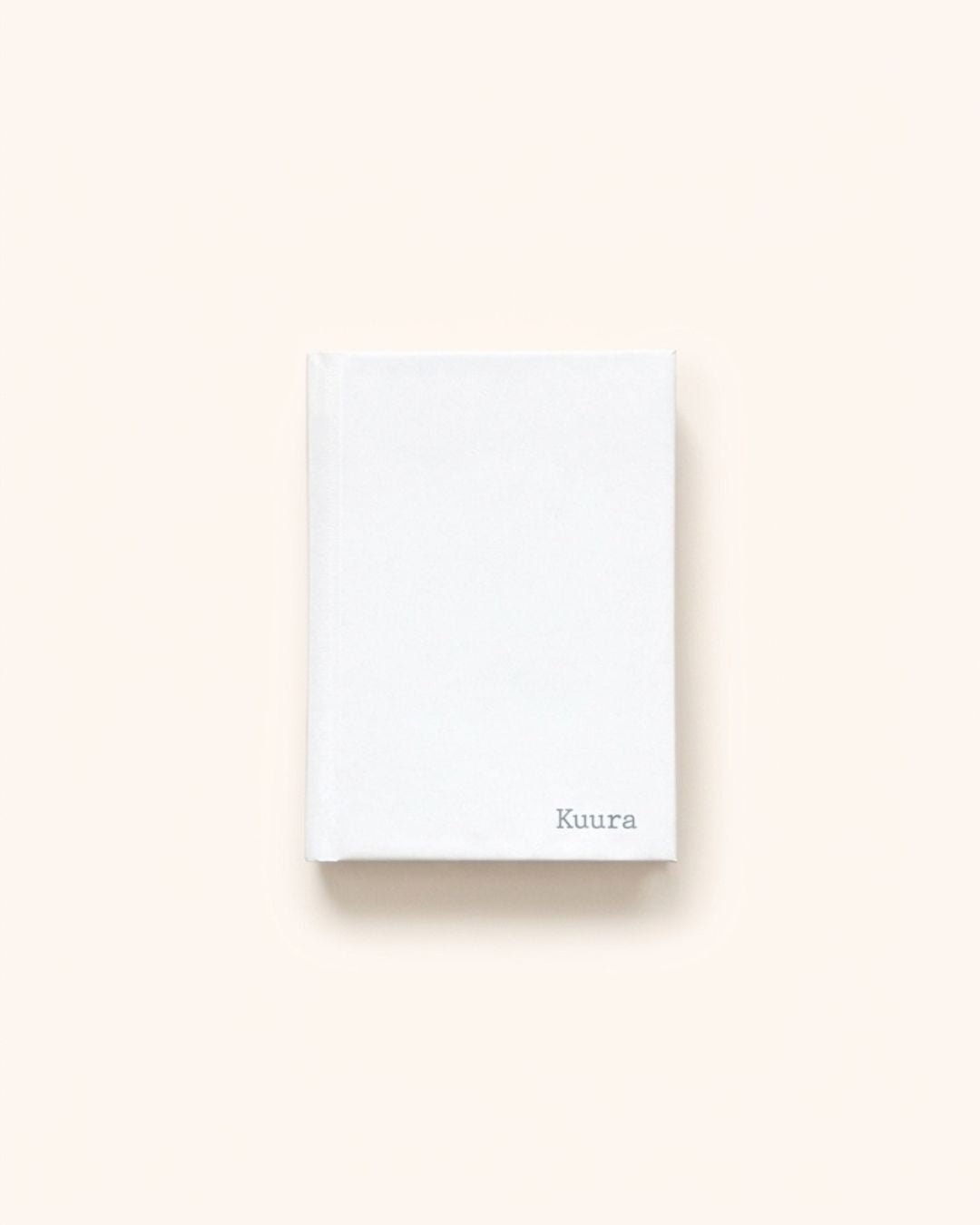 Flat lay photograph of the closed elegant white Kuura A5 & A6 Unlined Hardcover Notebook, showcasing its sturdy casing and delicate debossed brand logo in the bottom right corner. A minimalist and durable journal ideal for an aesthetic sanctuary for thoughts and dreams
