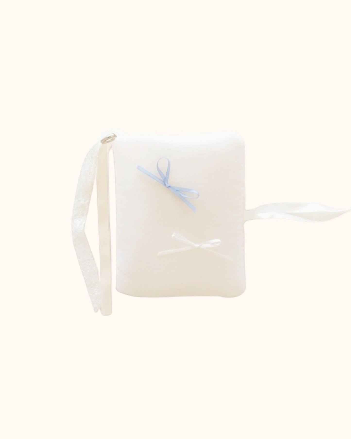 Close-up of the kuura Balloon A6 Journal & Notebook Cover with Pockets in a soft cream color. This kawaii puffy journal sleeve features a plush texture, decorated with delicate white and misty blue bows, complete with beautiful white lace and ribbon tie closures.