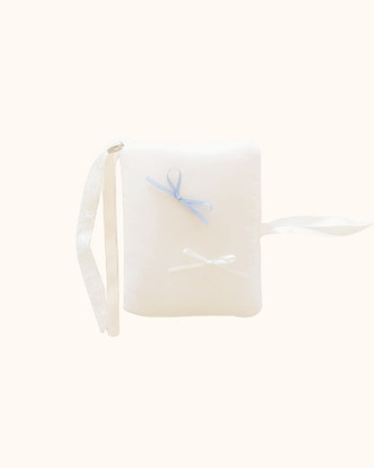 Close-up of the kuura Balloon A6 Journal & Notebook Cover with Pockets in a soft cream color. This kawaii puffy journal sleeve features a plush texture, decorated with delicate white and misty blue bows, complete with beautiful white lace and ribbon tie closures.