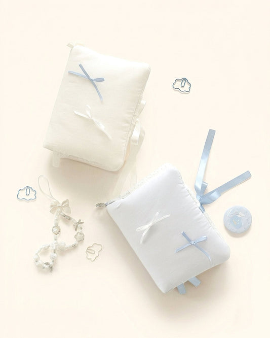 A flat lay aesthetic showcasing two Kuura Balloon puffy journal covers in misty blue and cream. The soft, pillowy A5 and A6 notebook sleeves are decorated with dainty satin bows, lace ribbons, and cute journaling accessories like cloud paper clips and a beaded charm. 