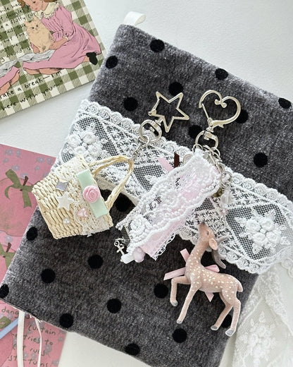 Kuura Little Meadow Charms, deer and picnic basket charms clipped onto a charcoal polka dot journal cover with white lace trim. Aesthetic journal decoration